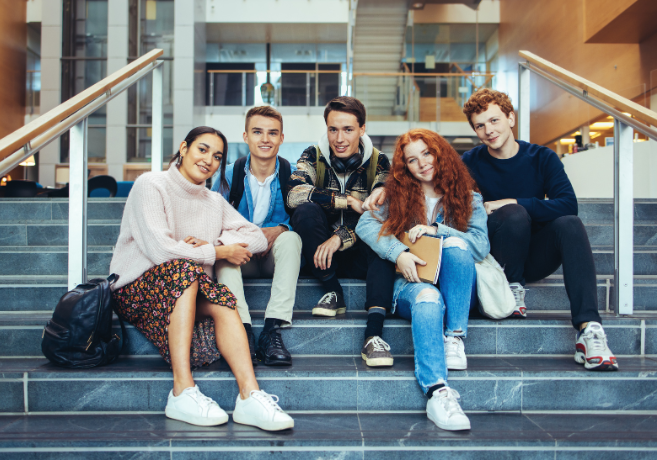 Studenter som sitter på en trapp i universitetet de studerer på. Smilende og blide.