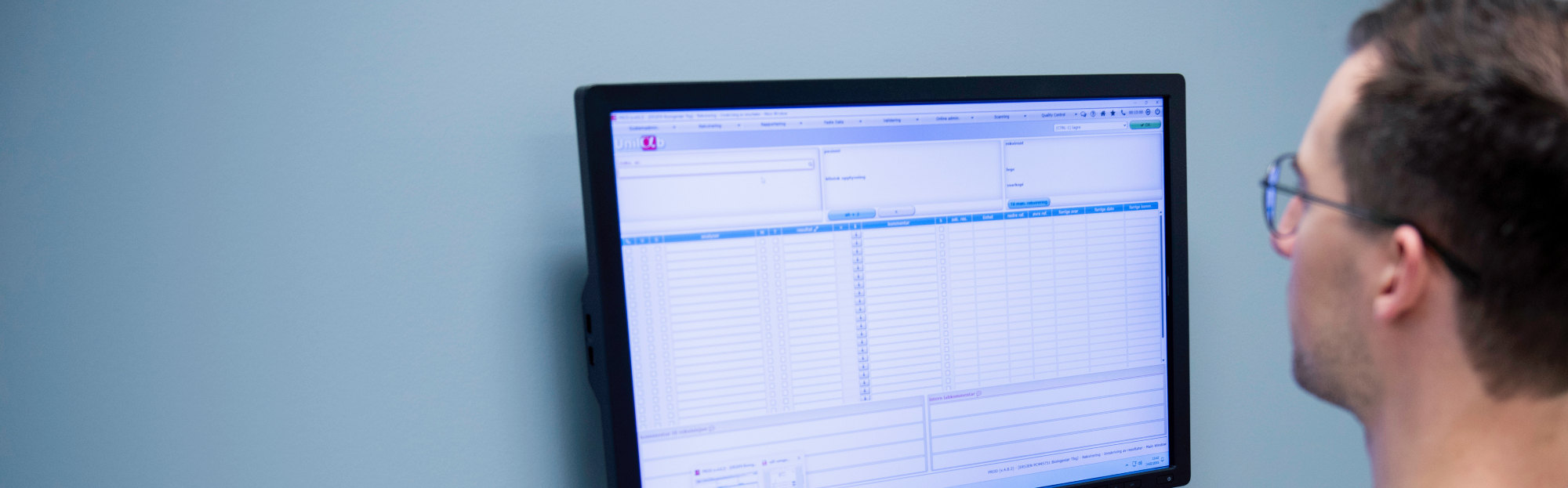 A computer screen shows a quality management system with tables and fields for laboratory data on a bright blue wall. Photo: Luca Kleve-Ruud