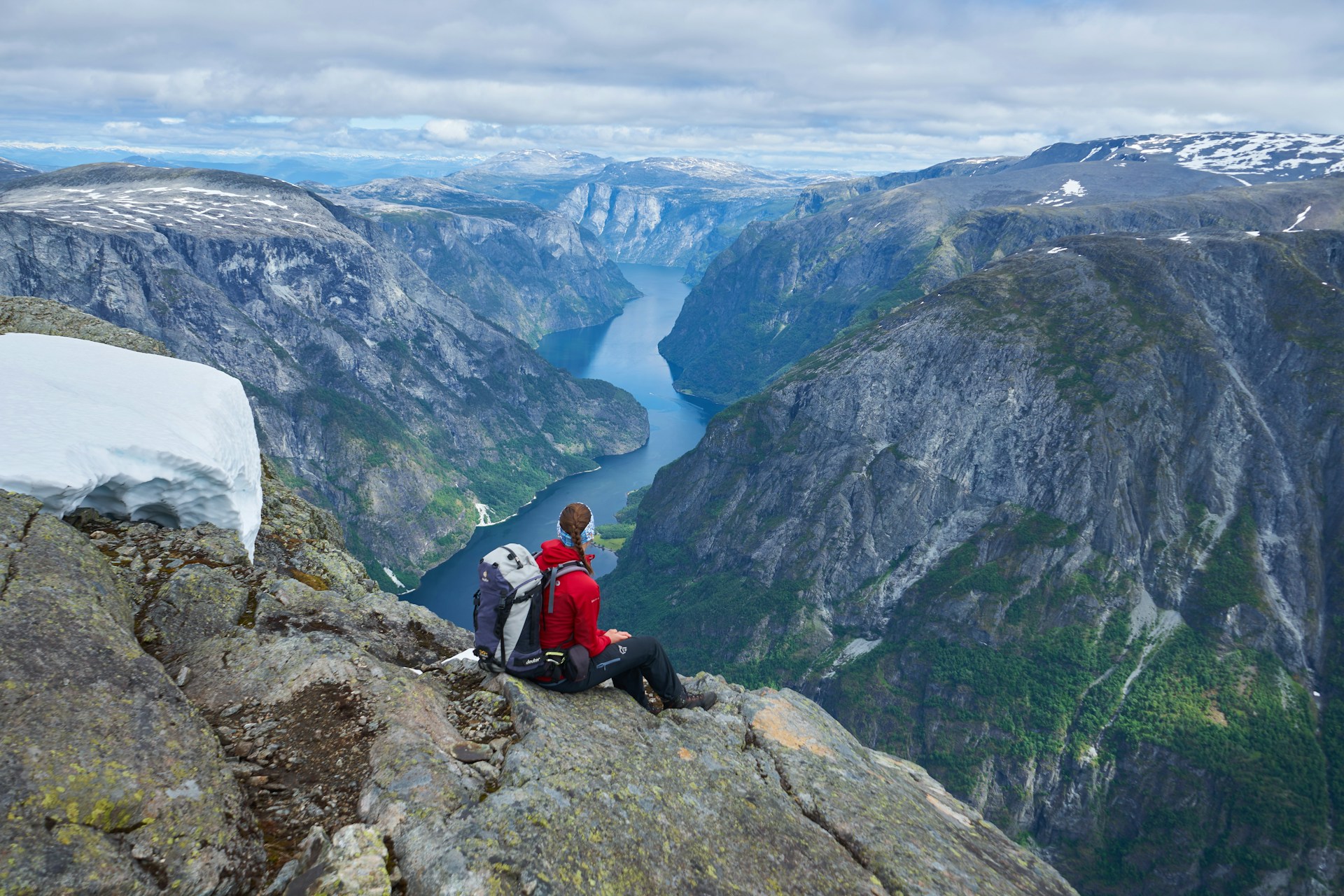 Bildet viser en turgåer med rød jakke og stor sekk som nyter utsikten over Nærøyfjorden fra toppen av fjellet Bakkanosi.