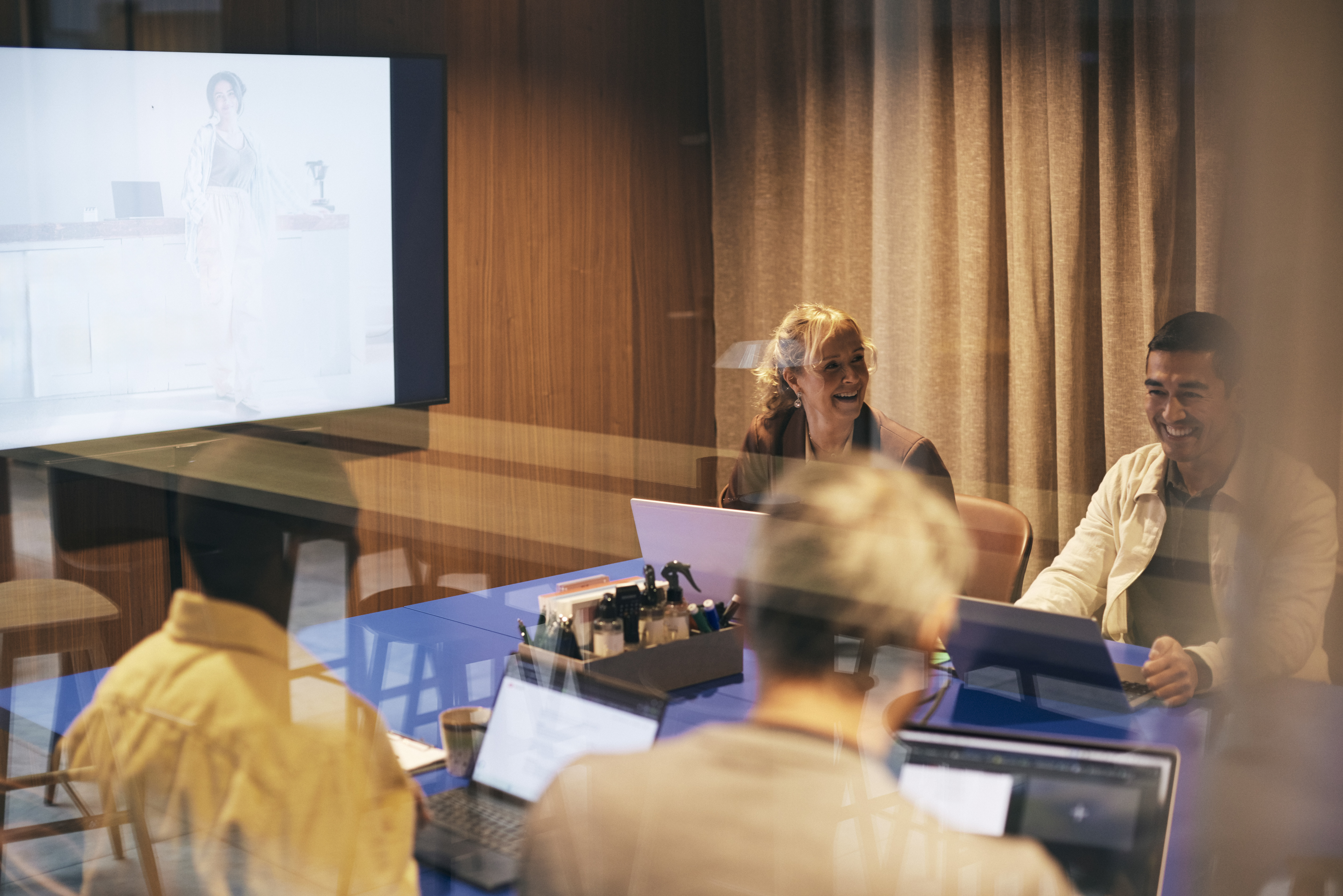 Internasjonalt samarbeidsmøte med smilende deltakere rundt et konferansebord, en person presenterer på storskjerm mens de andre følger med. Foto: GettyImages