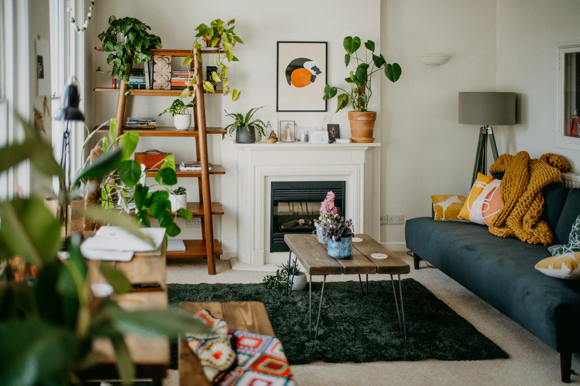 Lyst og moderne stueinteriør med grønne planter, sofa med puter og pledd, peis, og trebord med blomster på.