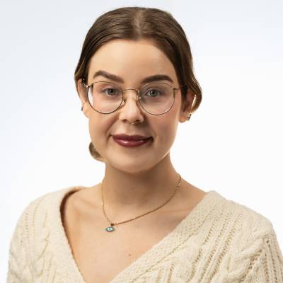 Portrett av en kvinne med runde briller, lys genser og oppsatt hår, tatt mot en nøytral bakgrunn.